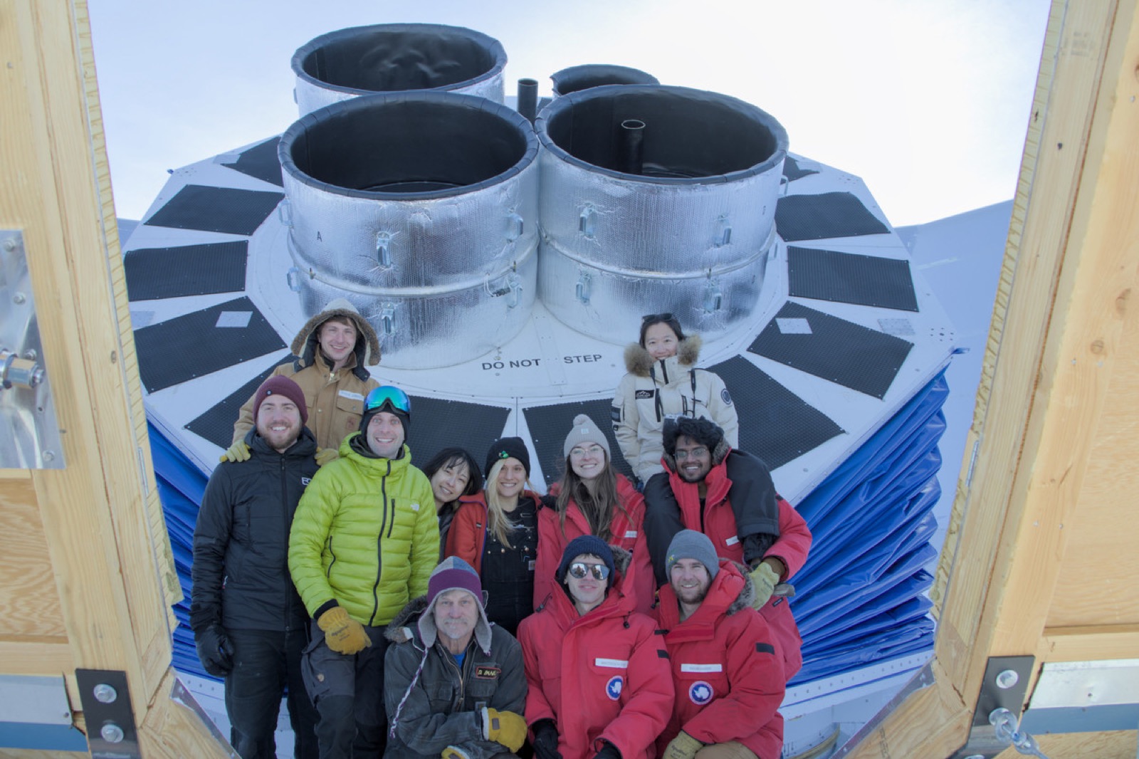 Eleven people in cold-weather gear posing in front of the four BICEP Array receiver windows.