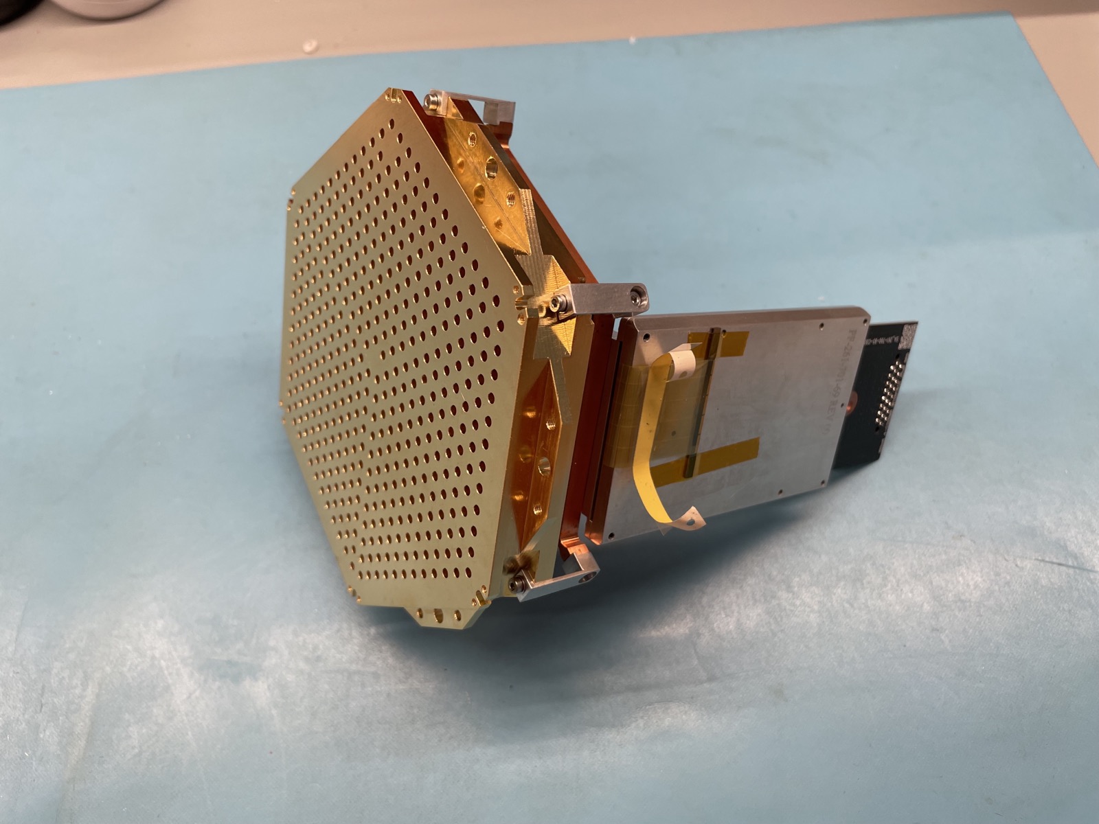 A hexagonal detector module standing on edge, its perforated feedhorn face at one end and its readout electronics and flexible cabling behind.