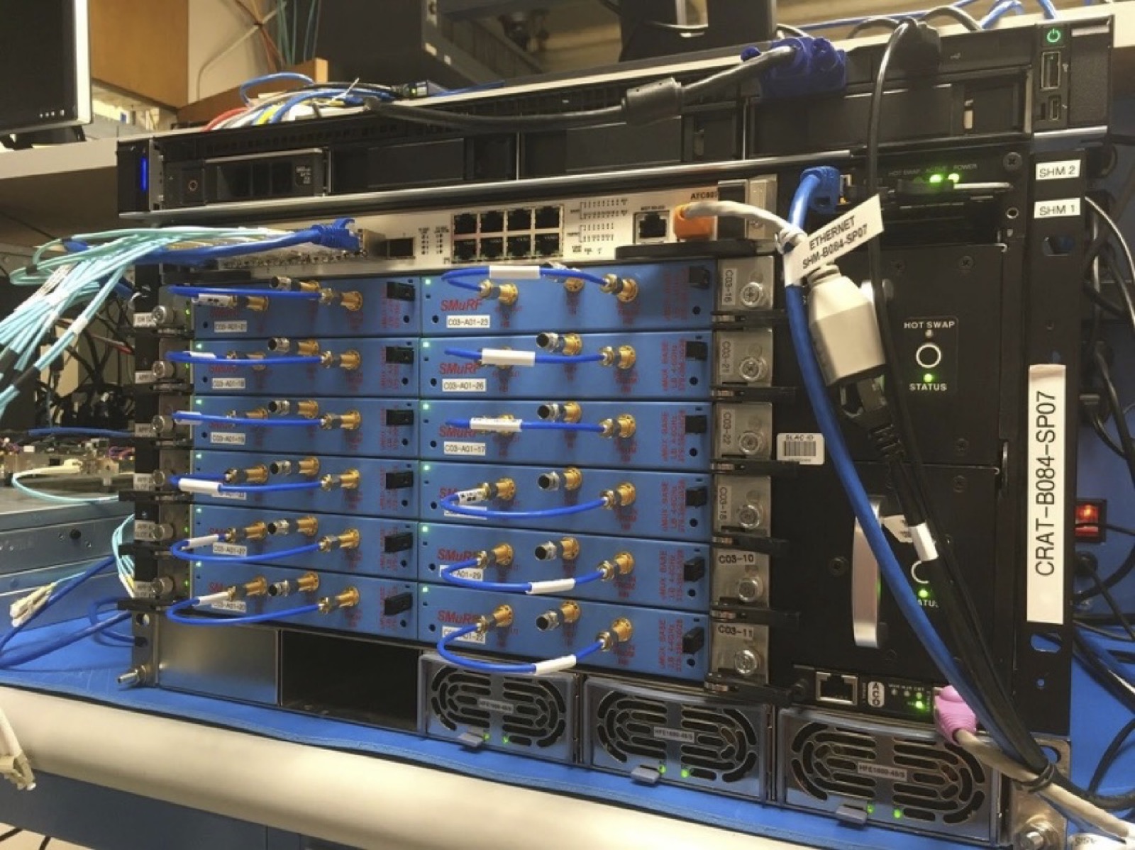 A rack-mounted crate holding six blue circuit cards, each with gold coaxial connectors and blue semi-rigid cables running to the left.
