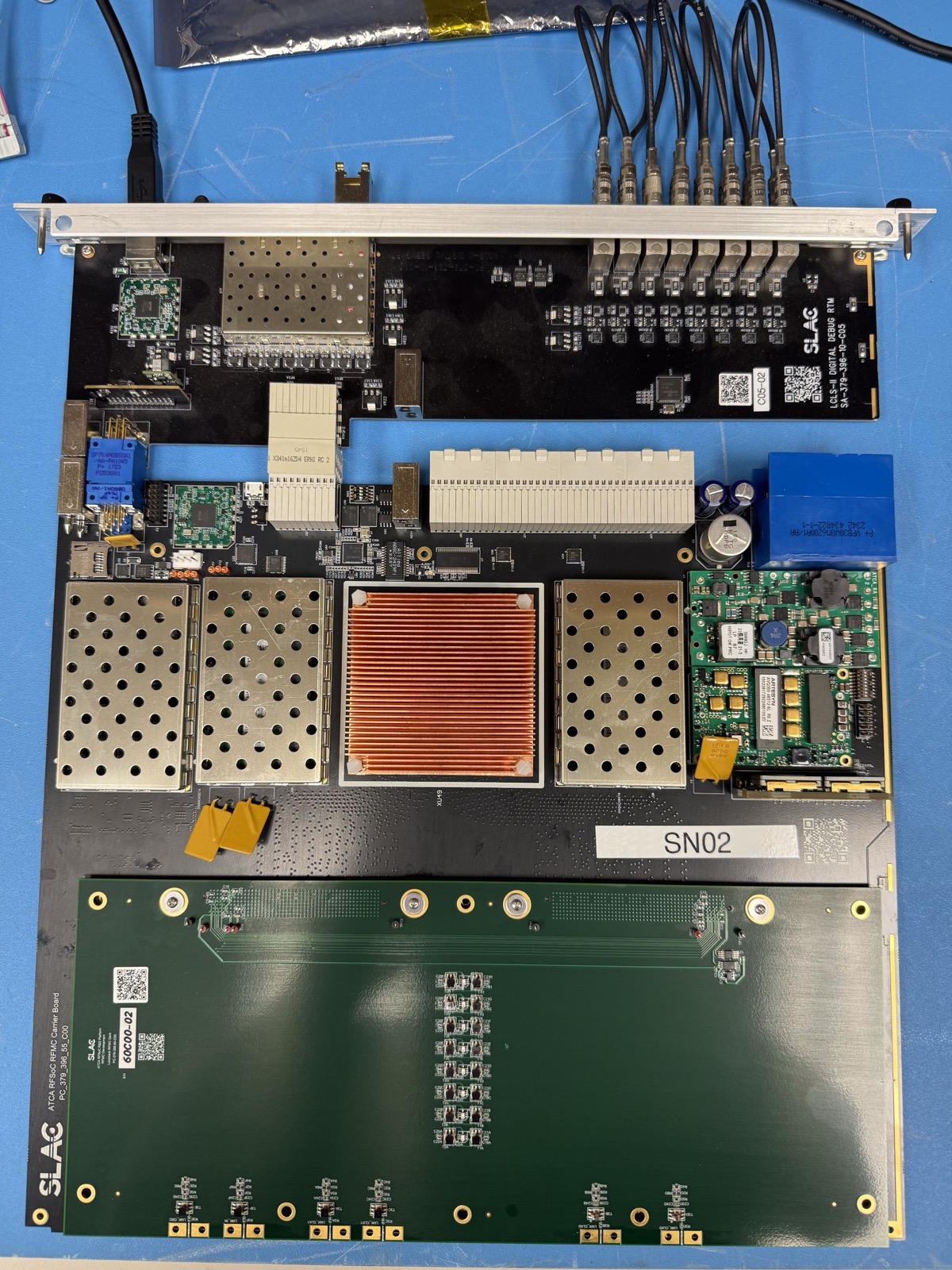 An RFSoC-based readout board on a blue bench mat, with shielded RF sections, a large copper heatsink and a row of coaxial connectors along the front panel.